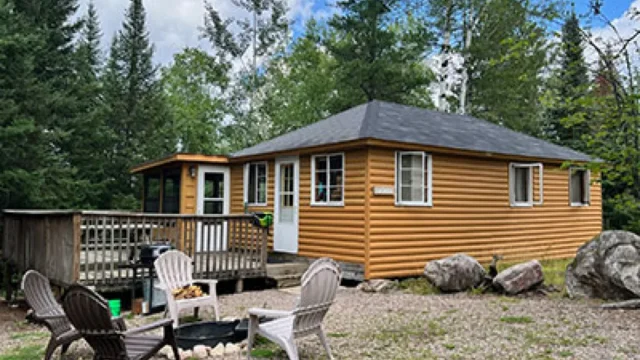 An outside view of the Alder cabin at Camp Northern Lights. It has a deck and lawn chairs around a fire pit.