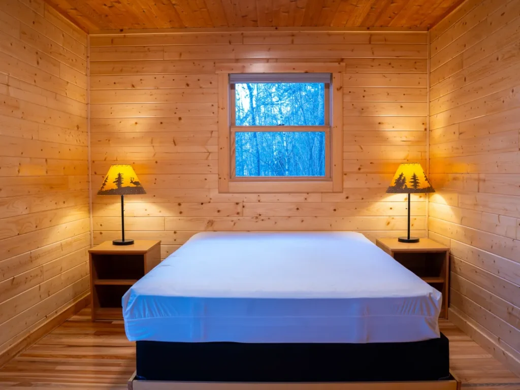 An inside view of one of the bedrooms in the Castillo Cabin. It has two night stands, two lamps, a queen size bed, and a window.