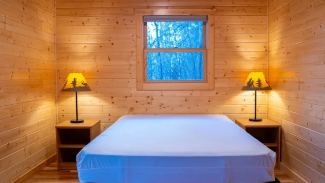An inside view of one of the bedrooms in the Castillo Cabin. It has two night stands, two lamps, a queen size bed, and a window.