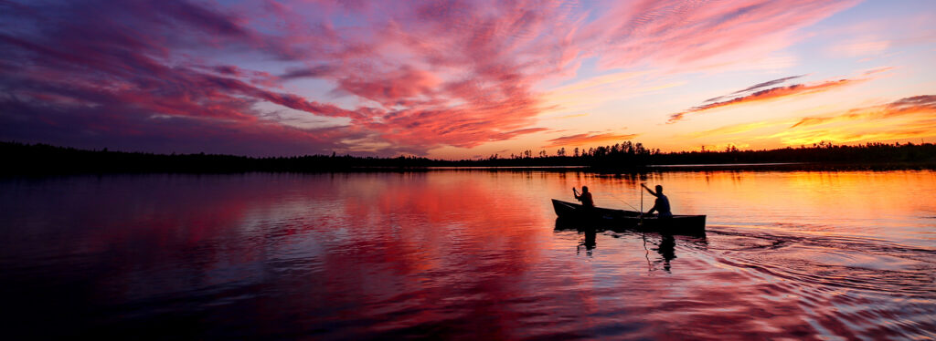 A canoe on the lake with a sunset at Camp Voyageur