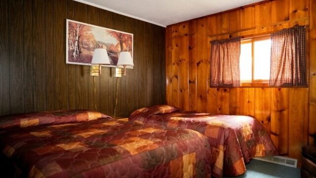 A view of one of the bedrooms in the Cedar cabin at Shagawa Beach Cabins. It has tow beds a queen and a full with two lamps for lighting.