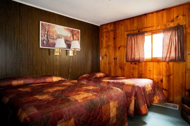 A view of one of the bedrooms in the Cedar cabin at Shagawa Beach Cabins. It has tow beds a queen and a full with two lamps for lighting.