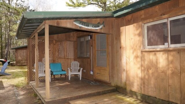 An outside view of the Cedar cabin at Shagawa Beach Cabins. It has a porch with deck chairs under an awning.