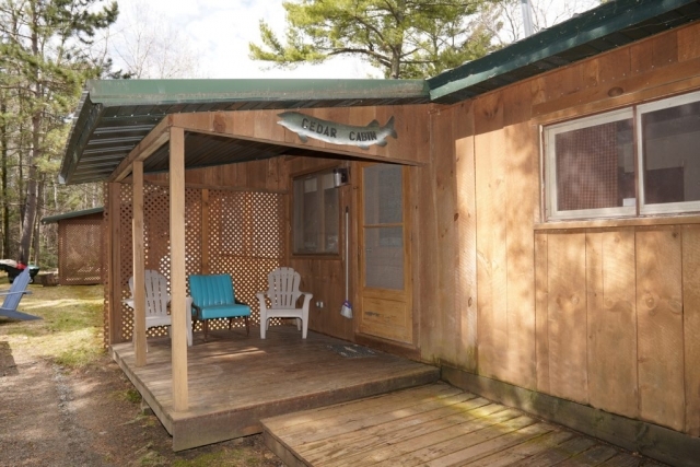 An outside view of the Cedar cabin at Shagawa Beach Cabins. It has a porch with deck chairs under an awning.
