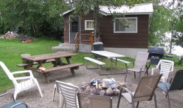 The outside of a cabin at Espland's Resort. There are chairs, a picnic table, and a firepit.