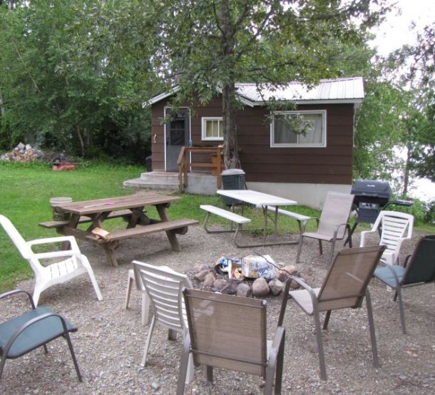 The outside of a cabin at Espland's Resort. There are chairs, a picnic table, and a firepit.