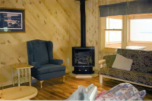The living room of one of the cabins at La Tourell's. It has a woodfire stove, a couch, a chair, and end tables.