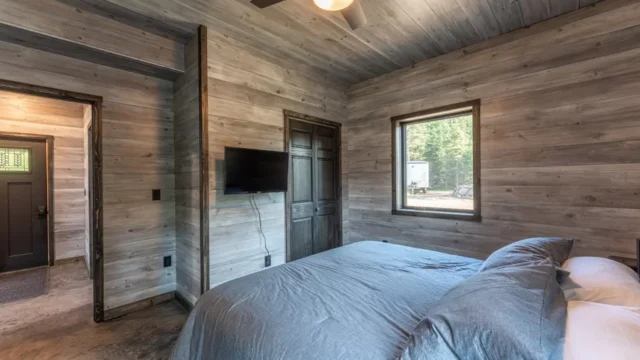 A view of one of the bedrooms at the North of North Resort. Featuring a large bed with a tv and medium sized window with light shining into the room.