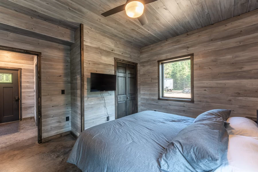 A view of one of the bedrooms at the North of North Resort. Featuring a large bed with a tv and medium sized window with light shining into the room.