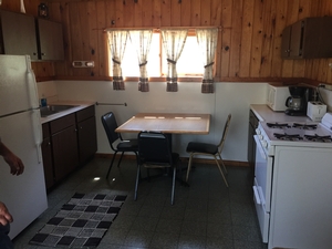 A view of the kitchen in one of the cabins at the Snowbank Lodge. It is a galley style kitchen with a refrigerator, stove, oven, microwave, coffee pot, and toaster.