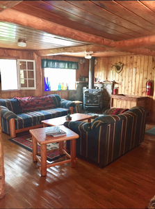 An inside view of the Snowbank Lodge it has couches, end tables, and woodfire stove.