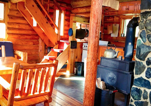 An inside view of the Triangle cabin. It has a table, woodfire stove, and a small kitchen.