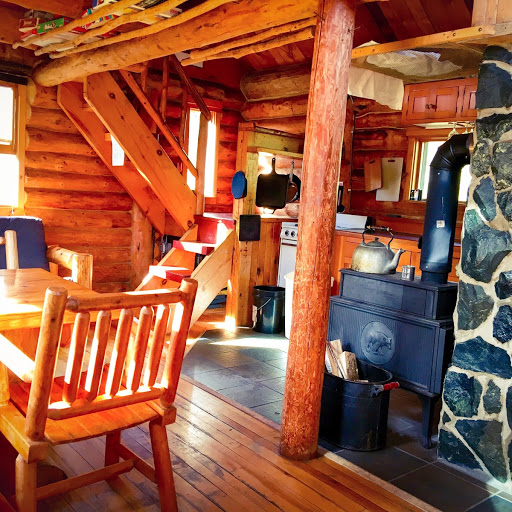 An inside view of the Triangle cabin. It has a table, woodfire stove, and a small kitchen.