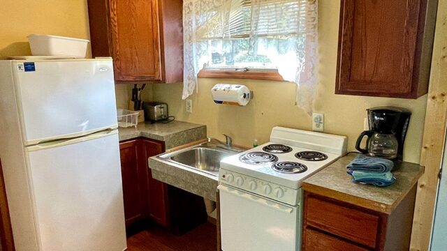 The kitchen of the one bedroom cabins at Veterans on the Lake Resort. It has a refrigerator, stove, oven, and coffee pot.