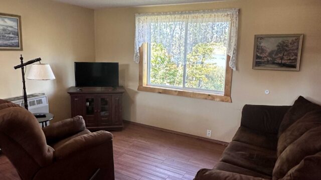 The living room of one of the one bedroom cabins at Veterans on the Lake Resort. There is a couch, a recliner, and a television in the room.