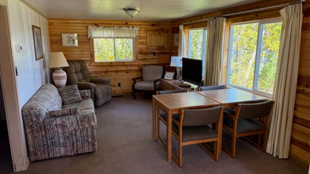 The living room of a two bedroom cabin at Veterans on the Lake Resort. It has a couch, recliner, tv, and table and chairs.