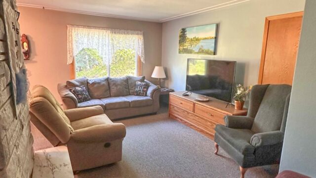 The living room of the 5 bedroom cabin at Veterans on the Lake Resort. It has a couch, recline, chair, and tv.