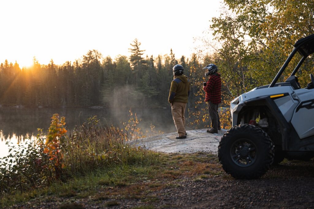 Image of two off-road riders standing outside their UTVs, admiring the forested fall scenery.
